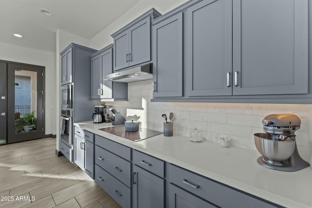 kitchen featuring under cabinet range hood, decorative backsplash, light countertops, and wood tiled floor