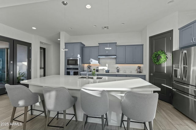 kitchen with a sink, decorative backsplash, stainless steel appliances, under cabinet range hood, and a kitchen bar