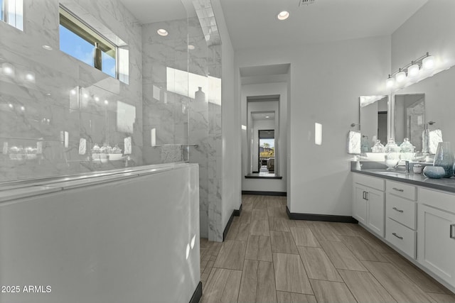 bathroom with a marble finish shower, vanity, and baseboards