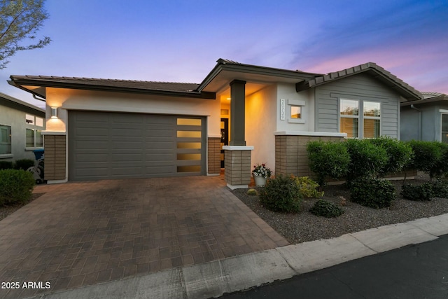 view of front of property featuring stucco siding, a tiled roof, decorative driveway, and a garage