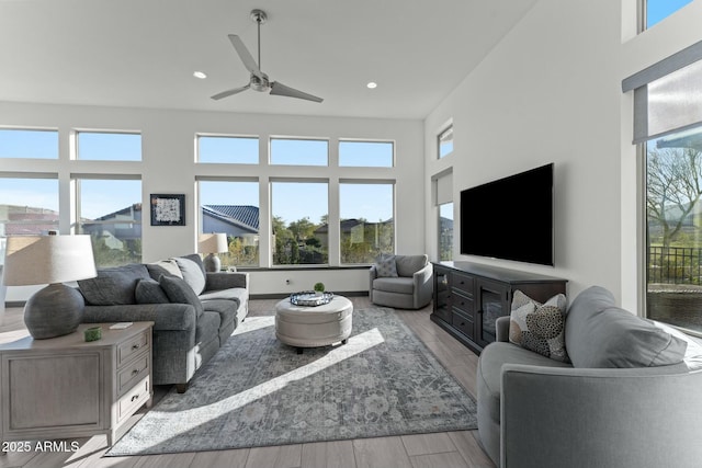 living area featuring recessed lighting, ceiling fan, light wood-style floors, and a towering ceiling