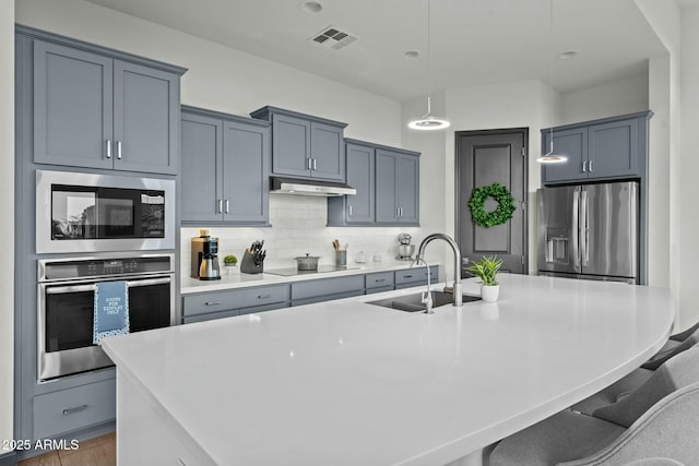 kitchen with visible vents, a large island with sink, a sink, stainless steel appliances, and backsplash