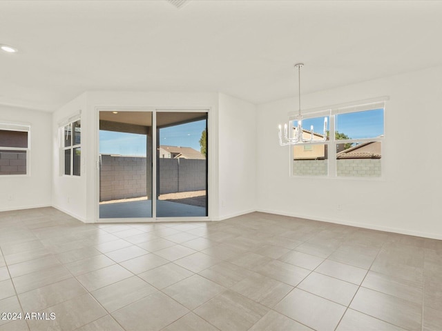 spare room featuring plenty of natural light, light tile patterned flooring, and an inviting chandelier