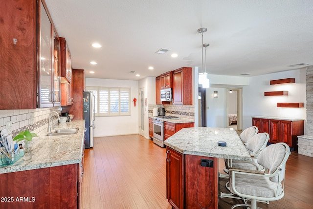 kitchen with appliances with stainless steel finishes, sink, light hardwood / wood-style flooring, light stone counters, and hanging light fixtures