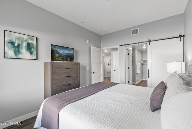 bedroom featuring baseboards, wood finished floors, a barn door, and a walk in closet