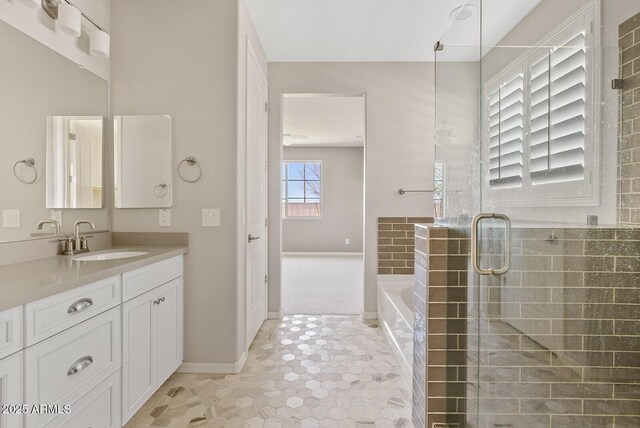 bathroom with vanity, a shower stall, a garden tub, and baseboards