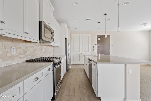 kitchen with tasteful backsplash, visible vents, light wood-type flooring, stainless steel appliances, and white cabinetry