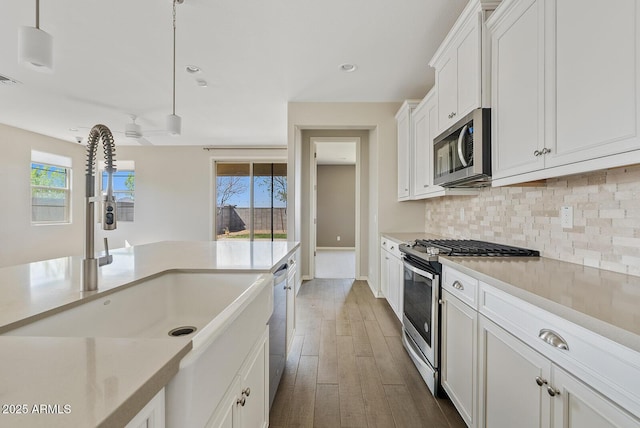 kitchen with a sink, backsplash, wood finished floors, stainless steel appliances, and white cabinets