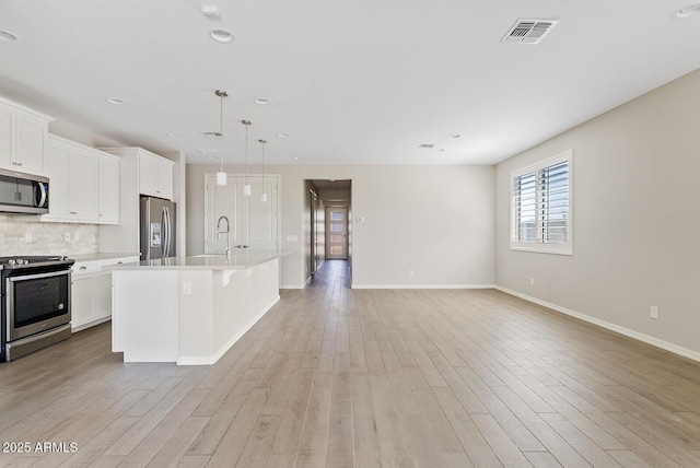 kitchen featuring visible vents, a kitchen island with sink, stainless steel appliances, tasteful backsplash, and light wood-type flooring