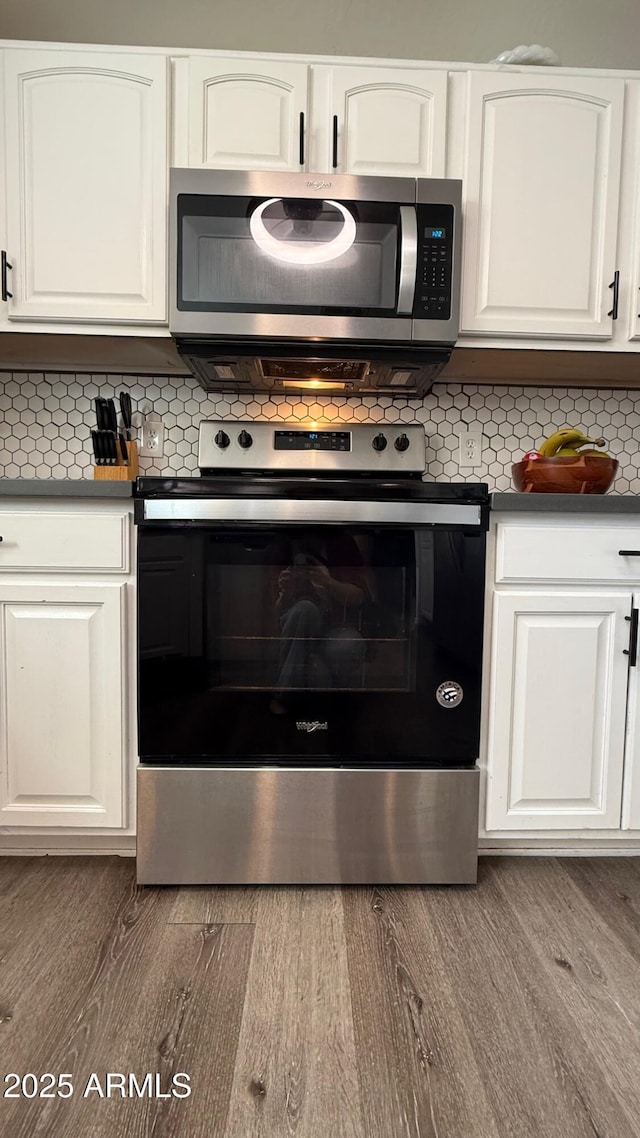 kitchen featuring tasteful backsplash, dark countertops, appliances with stainless steel finishes, wood finished floors, and white cabinets