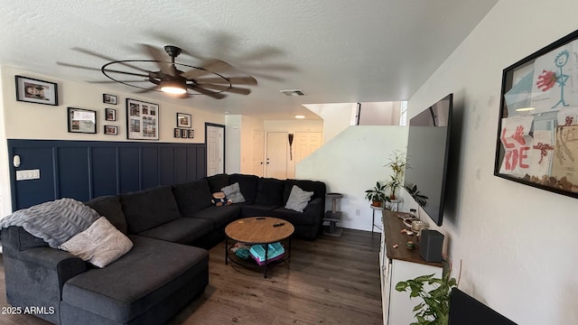 living area featuring dark wood-type flooring, a ceiling fan, visible vents, and a textured ceiling