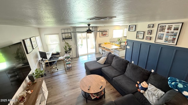 living area featuring a decorative wall, wood finished floors, a wainscoted wall, and a textured ceiling