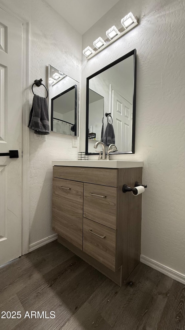 bathroom with vanity, wood finished floors, baseboards, and a textured wall