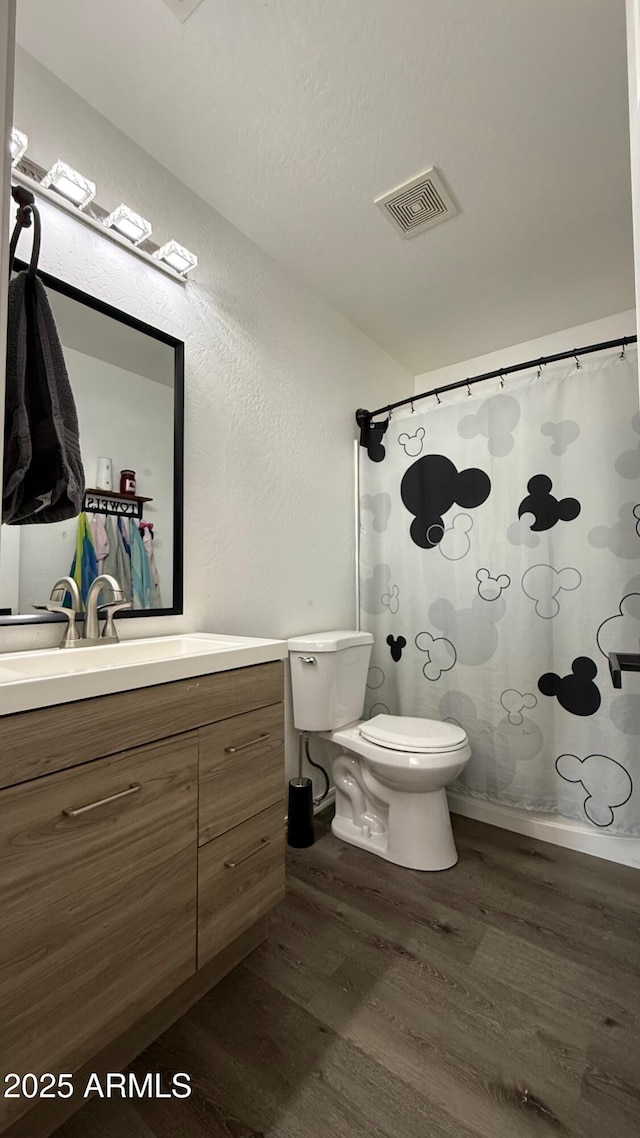 bathroom featuring vanity, wood finished floors, visible vents, toilet, and a textured wall