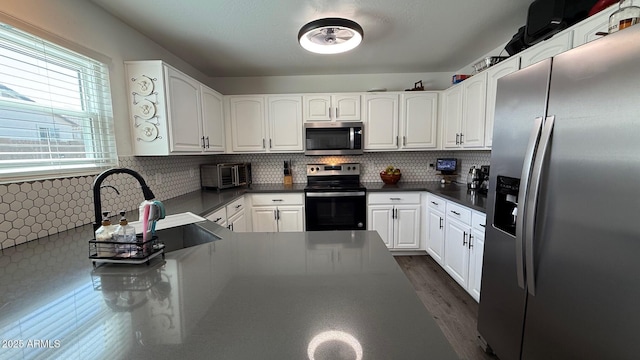 kitchen with decorative backsplash, dark countertops, appliances with stainless steel finishes, and white cabinetry