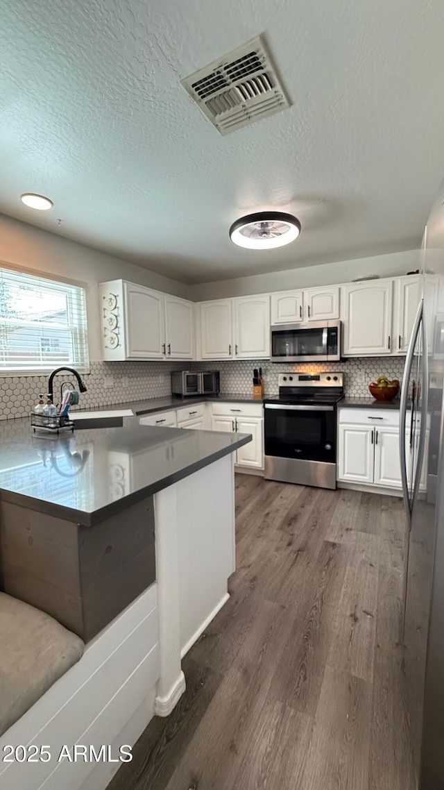 kitchen with dark countertops, visible vents, dark wood-type flooring, appliances with stainless steel finishes, and a sink