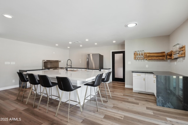 kitchen with a spacious island, sink, light hardwood / wood-style floors, white cabinetry, and stainless steel refrigerator