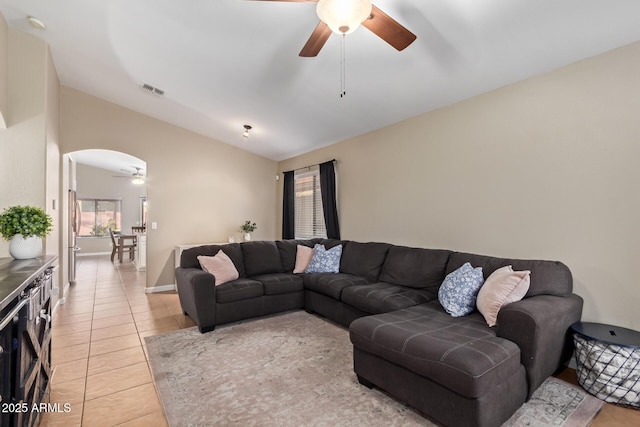 living area featuring light tile patterned floors, a ceiling fan, visible vents, lofted ceiling, and arched walkways