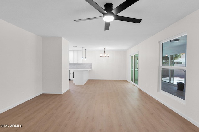 unfurnished living room featuring a chandelier, light wood-style flooring, a ceiling fan, and baseboards