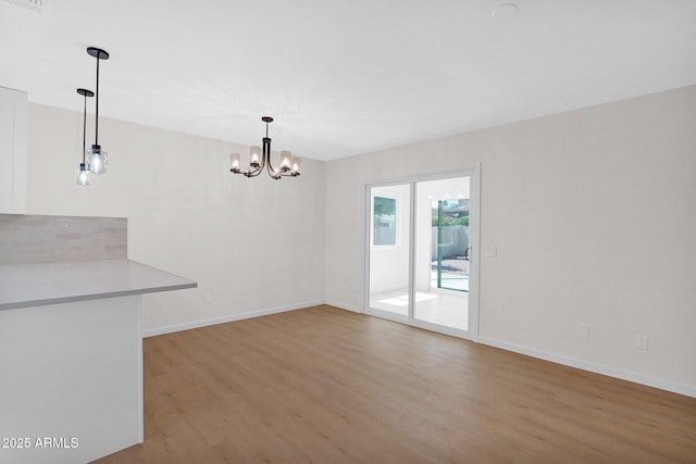 unfurnished dining area with light wood-style floors, a chandelier, and baseboards