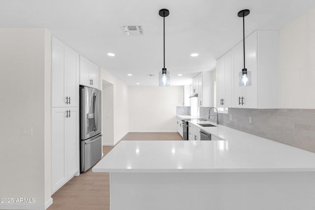kitchen with appliances with stainless steel finishes, light countertops, light wood-type flooring, a sink, and white cabinets