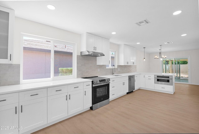 kitchen with appliances with stainless steel finishes, under cabinet range hood, light wood-style flooring, a peninsula, and white cabinetry