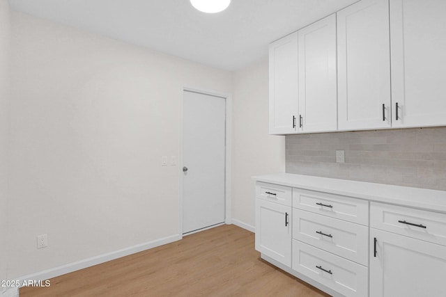kitchen featuring light wood finished floors, decorative backsplash, baseboards, and light countertops