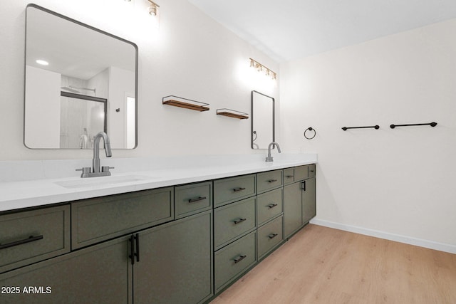 full bath featuring wood finished floors, double vanity, baseboards, and a stall shower