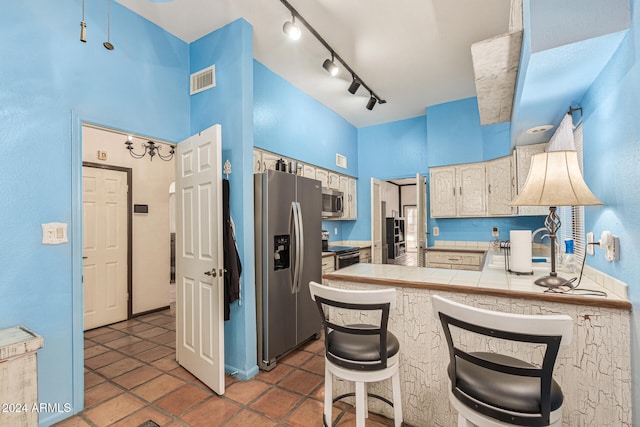 kitchen featuring appliances with stainless steel finishes, a towering ceiling, rail lighting, a kitchen breakfast bar, and tile counters