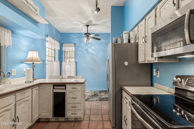 kitchen featuring tile countertops, ceiling fan, sink, and appliances with stainless steel finishes