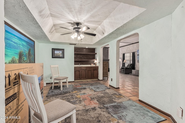 living area featuring a raised ceiling, ceiling fan, and tile patterned flooring