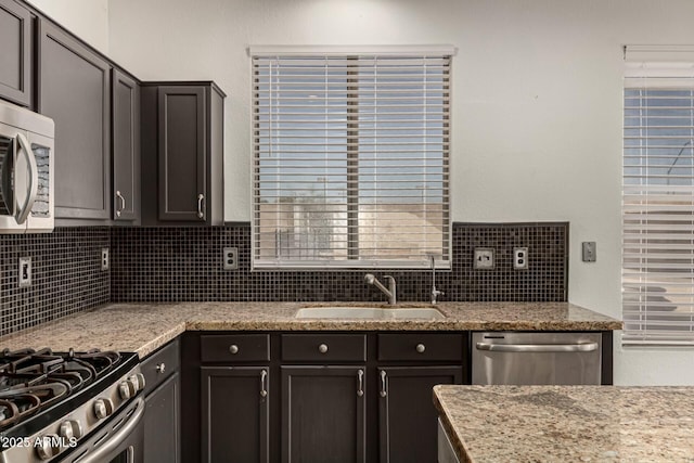 kitchen with backsplash, light stone counters, sink, and appliances with stainless steel finishes