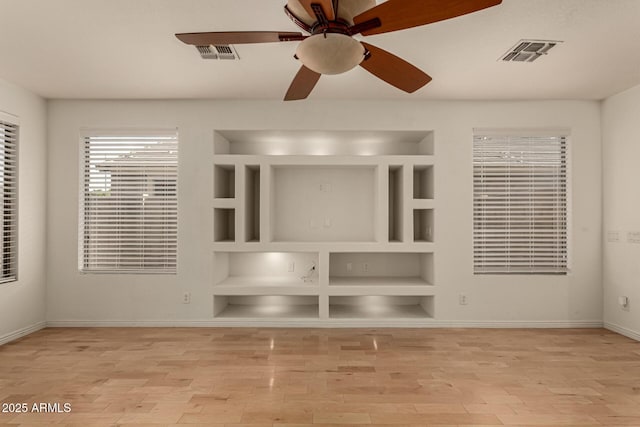 unfurnished living room with built in shelves, ceiling fan, and light hardwood / wood-style flooring