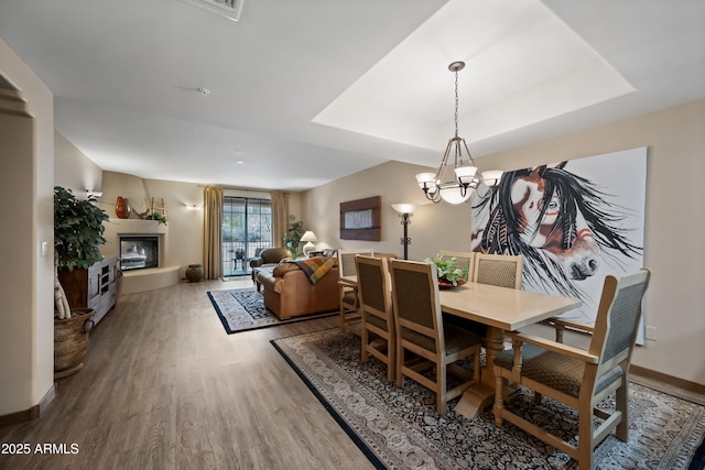 dining room with a glass covered fireplace, a raised ceiling, a notable chandelier, and wood finished floors