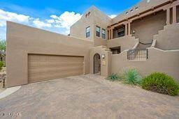 adobe home with an attached garage, driveway, and stucco siding