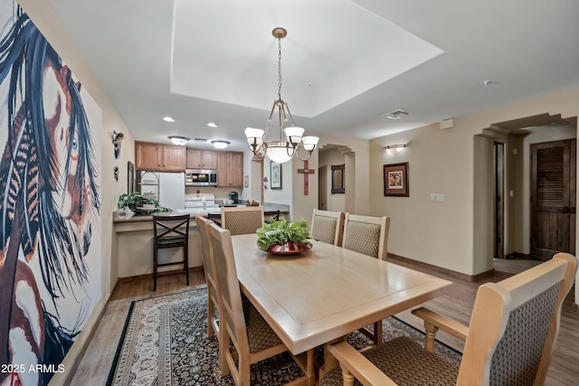 dining area with arched walkways, wood finished floors, visible vents, baseboards, and a tray ceiling