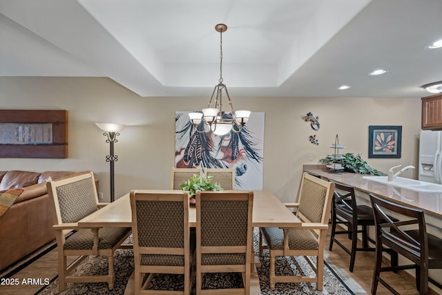 dining area with a chandelier, recessed lighting, a tray ceiling, and wood finished floors