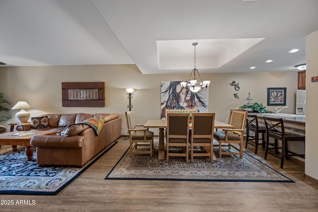 dining area featuring a tray ceiling, recessed lighting, wood finished floors, and a notable chandelier