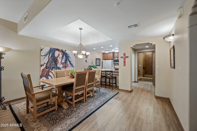 dining space with a tray ceiling, light wood-type flooring, visible vents, and baseboards