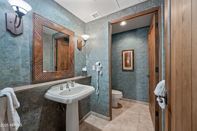 bathroom featuring toilet, a sink, visible vents, baseboards, and tile patterned floors