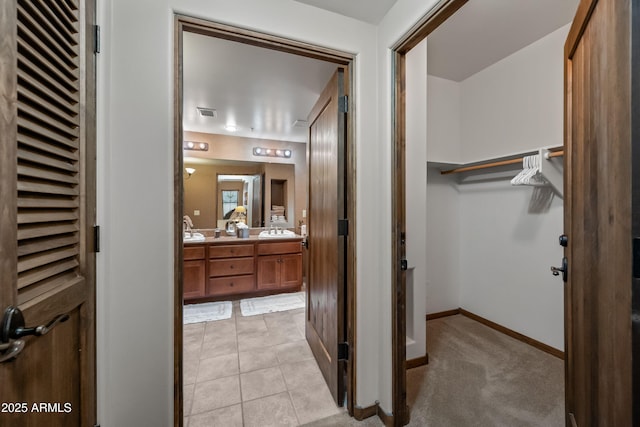 bathroom featuring double vanity, a spacious closet, a sink, baseboards, and tile patterned floors