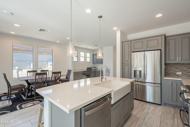 kitchen featuring pendant lighting, sink, gray cabinets, an island with sink, and stainless steel appliances