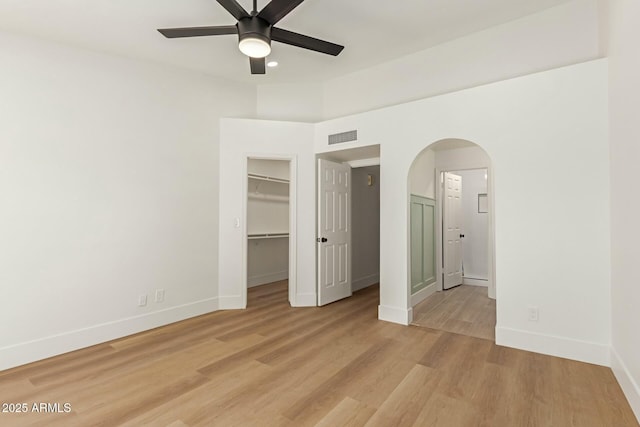 unfurnished bedroom with arched walkways, visible vents, a spacious closet, light wood-type flooring, and baseboards