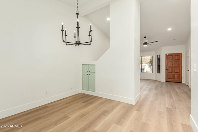 unfurnished dining area with ceiling fan with notable chandelier, high vaulted ceiling, light wood finished floors, and baseboards