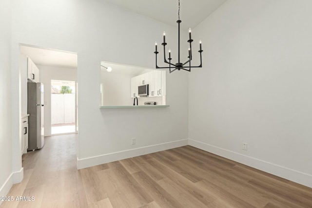 unfurnished dining area with light wood-type flooring, a notable chandelier, a towering ceiling, and baseboards