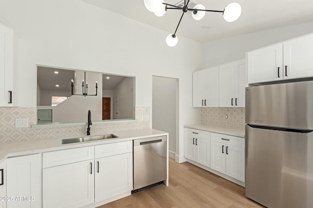 kitchen with stainless steel appliances, a sink, white cabinetry, light wood-style floors, and vaulted ceiling