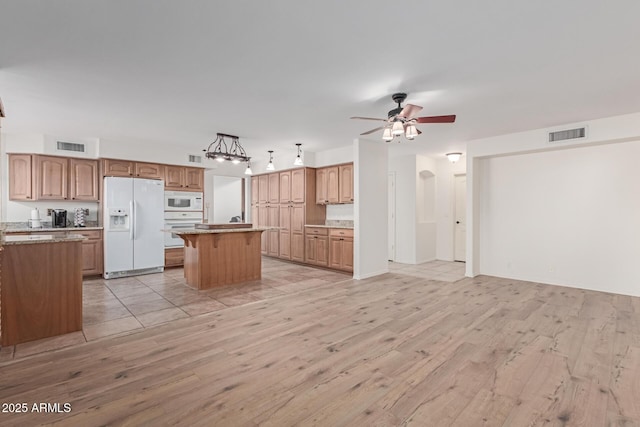 kitchen with white appliances, hanging light fixtures, light wood-type flooring, a kitchen island, and ceiling fan