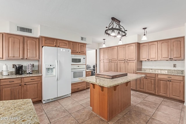 kitchen with light tile patterned floors, white appliances, hanging light fixtures, light stone countertops, and a kitchen island