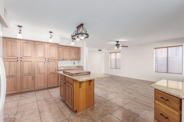 kitchen with pendant lighting, light stone countertops, a kitchen island, and light tile patterned floors