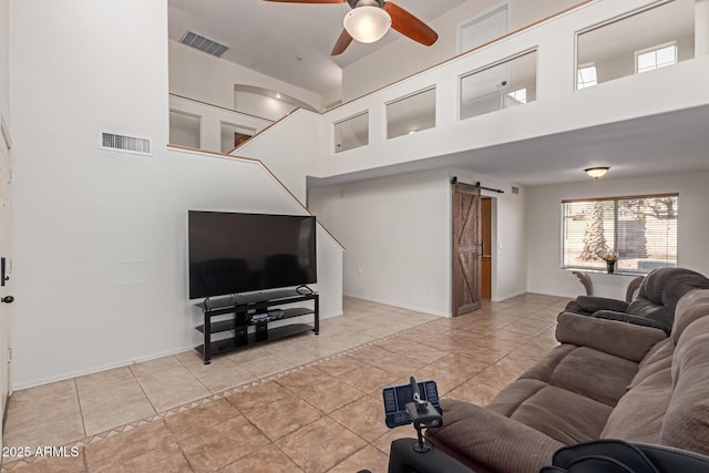 tiled living room with ceiling fan, a towering ceiling, and a barn door